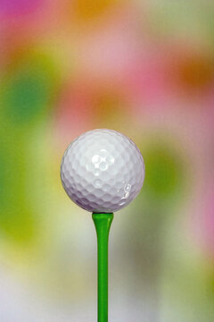 A plain white unbranded golf ball on a coloured 70mm tee peg in front of a multi-coloured background