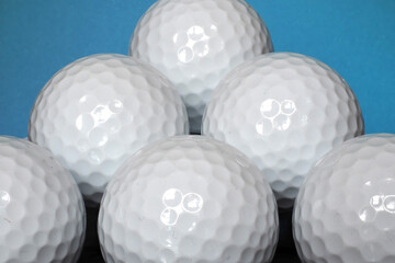 Close-up image of several plain white golf balls stacked up upon each other with a blue background
