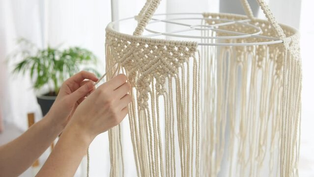 Woman making macrame lampshade with white threads at home. Woman knits ornament for lamp shade. Closeup shot. Macrame knitting concept.