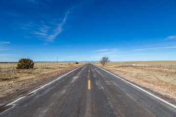 A long straight road through the New Mexico countryside, with a blue sky overhead - 748215583