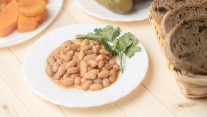 boiled beans in sauce in a white plate and a piece of greens, food Great Orthodox Lent