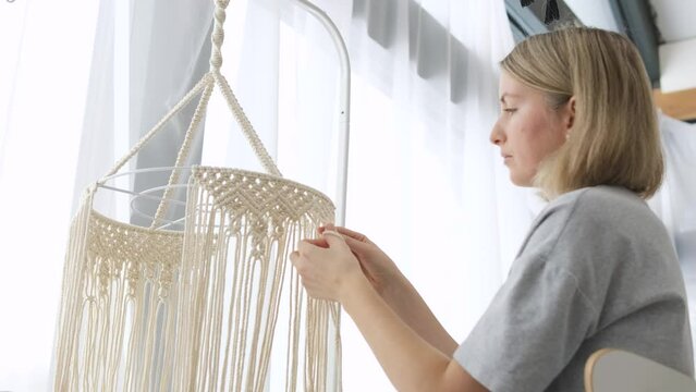 Woman making macrame lampshade with white threads at home. Woman knits ornament for lamp shade. Home hobby. Macrame knitting concept.