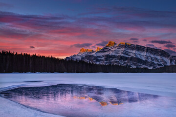 Golden sunrise at Two Jack Lake in Banff with alpenglow Rundle Mountain peaks reflecting off frozen lake