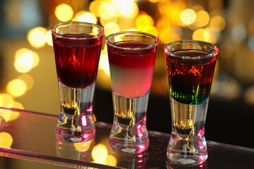 Different shooters in shot glasses on surface against blurred background, closeup Alcohol drink
