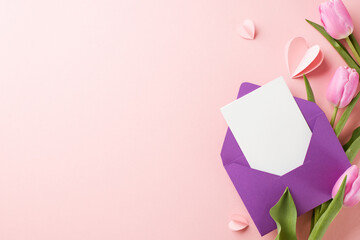 Mother's day charm: expressions of love. Top view shot of tulips, a purple envelope with a white card, paper hearts and  pink background with space for personalized messages