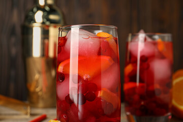 Tasty cranberry cocktail with ice cubes and orange in glasses on table, closeup