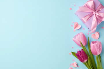 Mother's day surprise: joy in simplicity. Top view shot of tulips, paper hearts, and gift box with ribbon on a light blue background with space for loving messages and dedication
