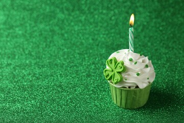 St. Patrick's day party. Tasty cupcake with clover leaf topper and burning candle on shiny green...