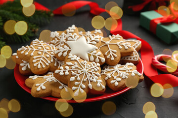 Tasty Christmas cookies with icing and red ribbon on black table