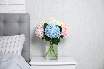 Beautiful hydrangea flowers in vase on white bedside table indoors