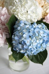 Beautiful hydrangea flowers in vase on white table, closeup