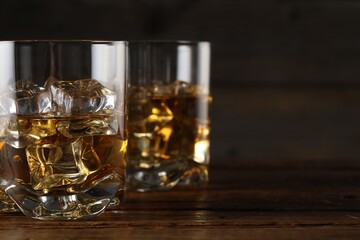 Whiskey with ice cubes in glasses on wooden table, closeup. Space for text