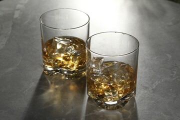 Whiskey with ice cubes in glasses on grey marble table
