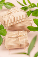 Craft cardboard recycled eco friendly gift boxes tied up with string bow on beige background among green plant leaves used as ecological zero waste holiday celebration present for birthday or wedding