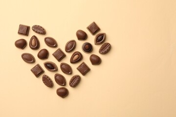 Heart made with delicious chocolate candies on beige background, top view. Space for text