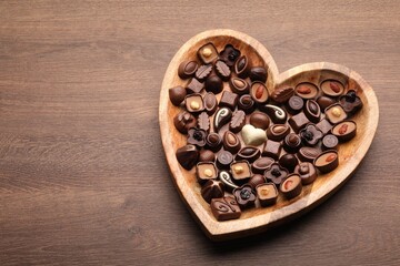 Heart shaped plate with delicious chocolate candies on wooden table, top view. Space for text