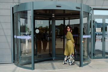 woman entering a supermarket. Caucasian model with long brunette hair, wears sunglasses and a khaki dress.