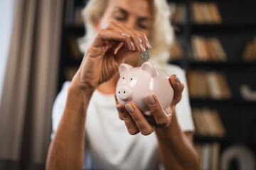 Saving money investment for future. Senior adult mature woman putting money coin in piggy bank. Old...