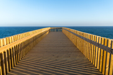 ein langer Holzsteg f&uuml;hrt in die Ferne und endet scheinbar in der Unendlichkeit der Zeit und ber&uuml;hrt fast den Horizont welcher aus dem blauen  Meer und dem blauen wolkenlosen Himmel besteht