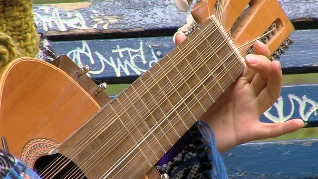 A Woman Playing A Typical Chilean Stringed Instrument Called "Chilean Guitarron" in a Park Bench. Close Up.