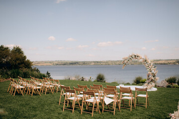 Natural minimalist wedding decor of white flowers and greenery on a green lawn with wooden chairs overlooking the water