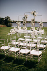 chiavari chairs. Outdoor wedding ceremony. wedding arch decorated with fresh white flowers with transparent chairs standing in the garden. Day of celebration, transparent chairs for guests