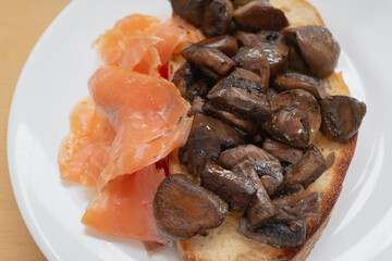 Fried mushrooms on sourdough toast with smoked salmon on a white plate seen from above. - 748246770