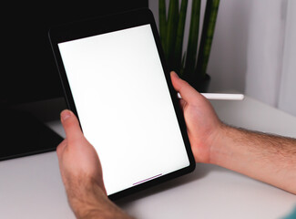 Mockup close-up man drawing of hand held with digital tablet white screen on home office in the living room. Concept of technology, connection, communication and freelance