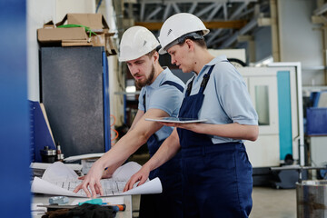 Professional drafter working in factory showing technical drawing to his female coworker, medium shot