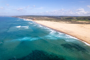ein beliebter Strand mit Wellen für Surfer an der Atlantikküste von Portugal bei schönem Wetter aus der Vogelperspektive über dem Meer