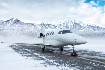 White corporate business jet at winter airport apron on the background of high scenic snow capped mountains