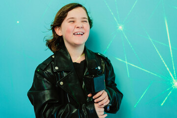 Cheerful child in a leather jacket laughs while holding a microphone, with a glowing turquoise backdrop giving a party vibe