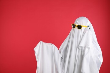 Person in ghost costume and sunglasses talking on smartphone against red background, space for text