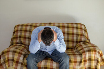 Image of a man sitting on a sofa while covering his ears and not wanting to hear anyone. Anxiety and depression problems.
 - obrazy, fototapety, plakaty