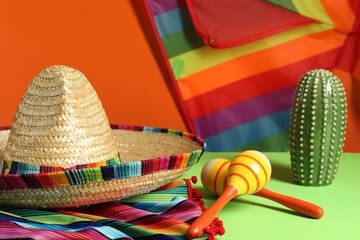 Composition with Mexican sombrero hat and maracas on green table, closeup