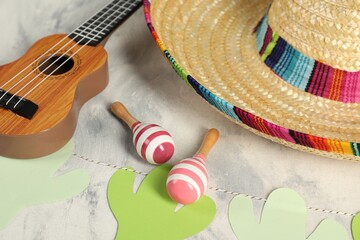 Mexican sombrero hat, ukulele and maracas on grey textured table, closeup
