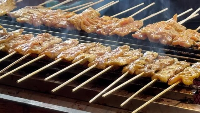 pork meat skewers in a local street market with customers walking in thailand	