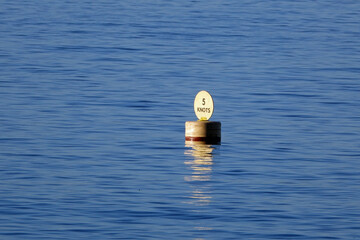 A yellow 5 Knots speed indicator buoy floating on a calm sea indicates the maximum speed at which...