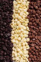 Dark, white and medium dark chocolate drops for making chocolate, candies, cakes as a background. Tempered chocolate confectionery concept. Chocolate background.