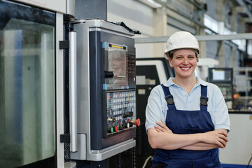 Medium portrait of successful female turner standing with arms crossed in factory workshop smiling...