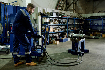 Long shot of man wearing blue uniform working with industrial equipment in modern workshop