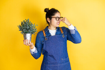 Young caucasian gardener woman holding a plant isolated on yellow background smelling something...