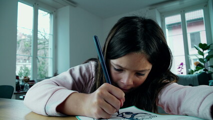 Focused Young Girl Drawing Creatively on Paper. A little girl deeply engaged in artistic play,...