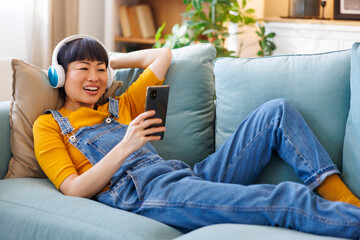 Woman wearing headset and using smart phone while relaxing at home