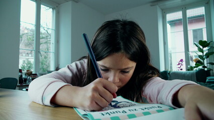 Focused Young Girl Drawing Creatively on Paper. A little girl deeply engaged in artistic play,...