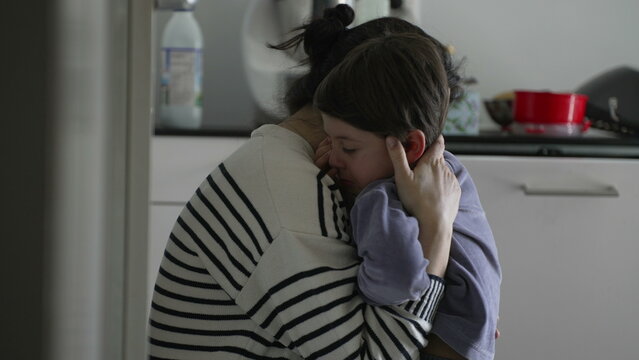 Mother consoling crying hurt little boy, candid tender moment of caring parent giving an empathic hug to upset child struggling with adversity, authentic and real life