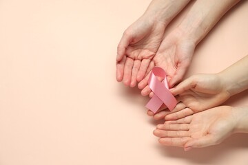 Breast cancer awareness. Women holding pink ribbon on beige background, top view. Space for text