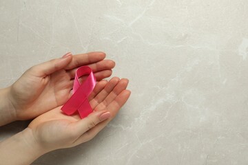 Breast cancer awareness. Woman with pink ribbon at light grey table, top view. Space for text