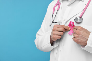 Mammologist with pink ribbon and stethoscope on light blue background, closeup. Space for text