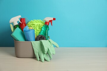 Different cleaning products in basket on wooden table against light blue background, space for text